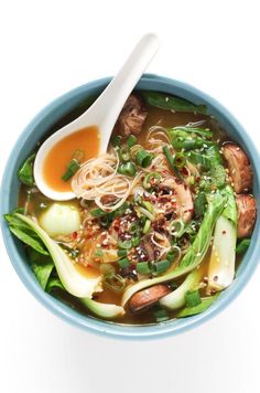 a blue bowl filled with noodle soup next to broccoli and carrots