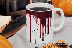 a coffee mug with blood dripping on it next to cookies and pumpkins in the background