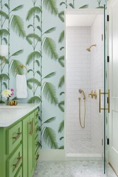 a bathroom with palm leaves on the wall and green cabinetry, along with a walk in shower