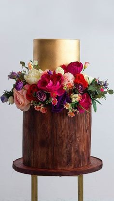 a three tiered cake decorated with colorful flowers on a wooden stand in front of a white wall