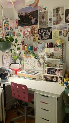 a desk with some pictures on the wall and a chair in front of it next to a potted plant