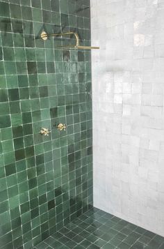 a green tiled shower with brass fixtures