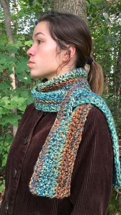 a woman wearing a brown jacket and blue scarf standing in front of trees with her back turned to the camera