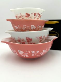 three pink and white bowls stacked on top of each other in front of a black box