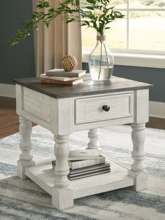 a white end table with books and a vase on it in front of a window