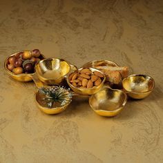 gold bowls filled with nuts and other food items on a brown tableclothed surface