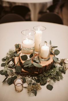 candles and greenery sit on top of a wood slice at a wedding reception table