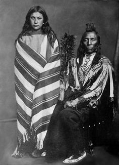 an old photo of two people dressed in native clothing