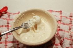 a person holding a fork in a bowl filled with whipped cream and other items on a red and white checkered table cloth