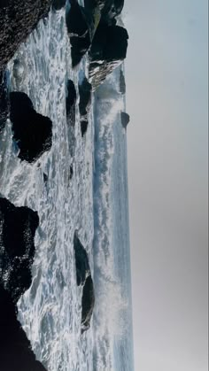 a man standing on the side of a cliff next to a body of water with waves crashing against it