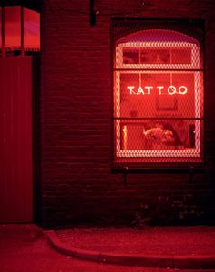 a red neon sign that reads tattoo on the side of a brick building at night