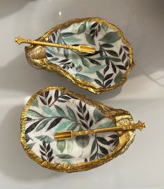 two pieces of decorative porcelain with gold trimmings and leaves on them, sitting side by side