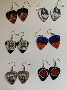 six guitar picks are hanging from hooks on a white surface, each with different designs