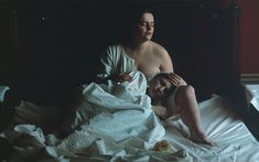 a woman sitting on top of a bed covered in white sheets