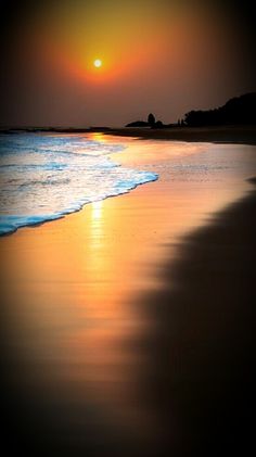 the sun is setting over the water at the beach with its reflection in the wet sand