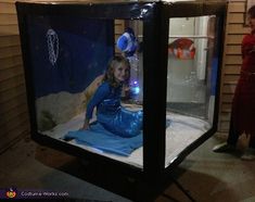 two children standing in front of a display case with an image of a mermaid on it