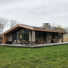 a modern house with an outdoor deck and picnic table in the grass near some trees