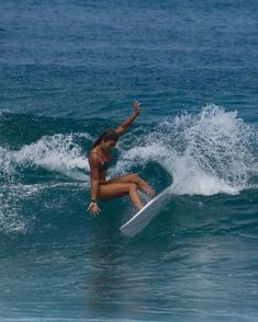 a woman riding a surfboard on top of a wave in the ocean with her arms up