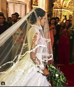 the bride is walking down the aisle in her wedding dress with veil over her head