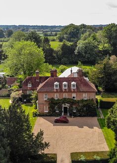 an aerial view of a large house surrounded by lush green trees and bushes, with a car parked in the driveway