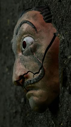 a creepy looking mask hanging from the side of a wall with dirt all over it