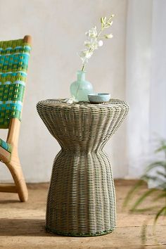 a wicker table with a vase on it and a chair in the back ground