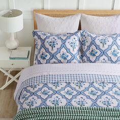 a bed with blue and white comforter on it next to a night stand in a bedroom