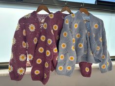 two knitted sweaters hanging on a window sill with sunflowers all over them