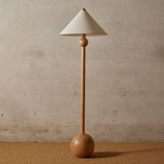 a wooden table lamp with a white shade on the base and a brown floor mat