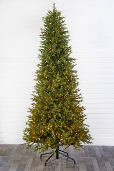 a christmas tree with lights on it in front of a white wall and wooden floor