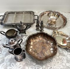 an assortment of antique silver ware on a lace tablecloth with serving dishes and trays