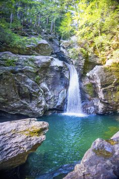 a waterfall in the middle of a forest with rocks and trees around it, surrounded by green water