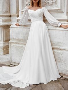 a woman in a white wedding dress leaning against a wall with her hands on her hips