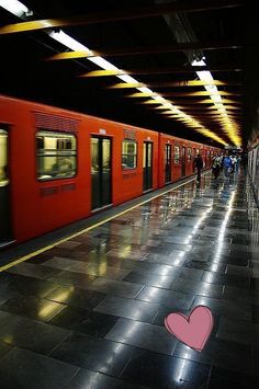 a red train with a pink heart on the side is pulling into a subway station