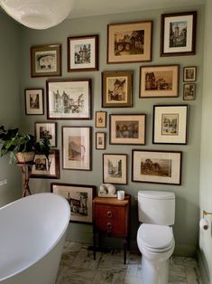 a white toilet sitting next to a bath tub in a bathroom under pictures on the wall