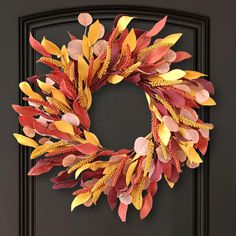 a wreath made out of paper leaves on a black front door with the words autumn written across it