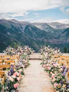 an outdoor ceremony setup with wooden chairs and flowers on the aisle, overlooking mountains in the distance