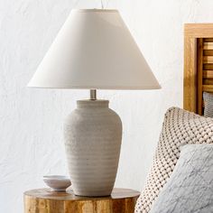 a white lamp sitting on top of a wooden table next to a bed with pillows