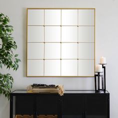 a large mirror on the wall above a black cabinet with candles and a plant in it