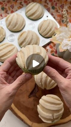 a person holding a cupcake in front of a muffin tin filled with frosting