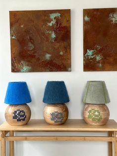 three lamps are sitting on a table in front of two paintings, one is gold and the other is blue