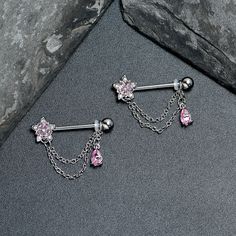 two piercings with pink stones on them sitting next to a stone wall and rock