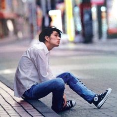 a young man sitting on the side of a street