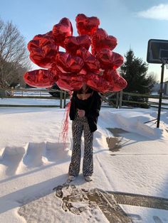 a woman standing in the snow next to a bunch of red foil heart shaped balloons