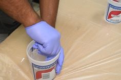 a man in blue gloves and rubber gloves painting a table with white paint on it