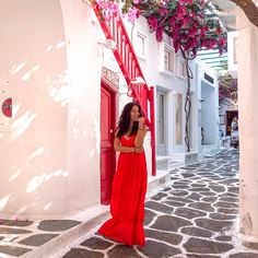 a woman in a long red dress is standing on the street and talking on her cell phone