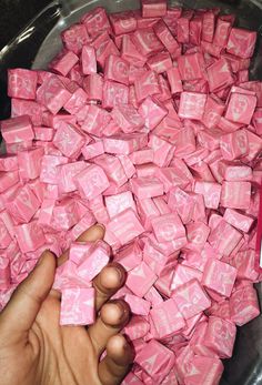 a person is reaching for pink candy cubes in a bowl