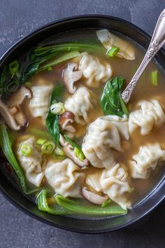 a black bowl filled with dumplings and green vegetables on top of a gray table