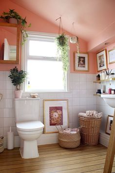 a white toilet sitting next to a window with pictures on the wall and plants hanging above it