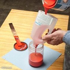 a person pouring red liquid into a jar on top of a wooden table next to a pair of scissors